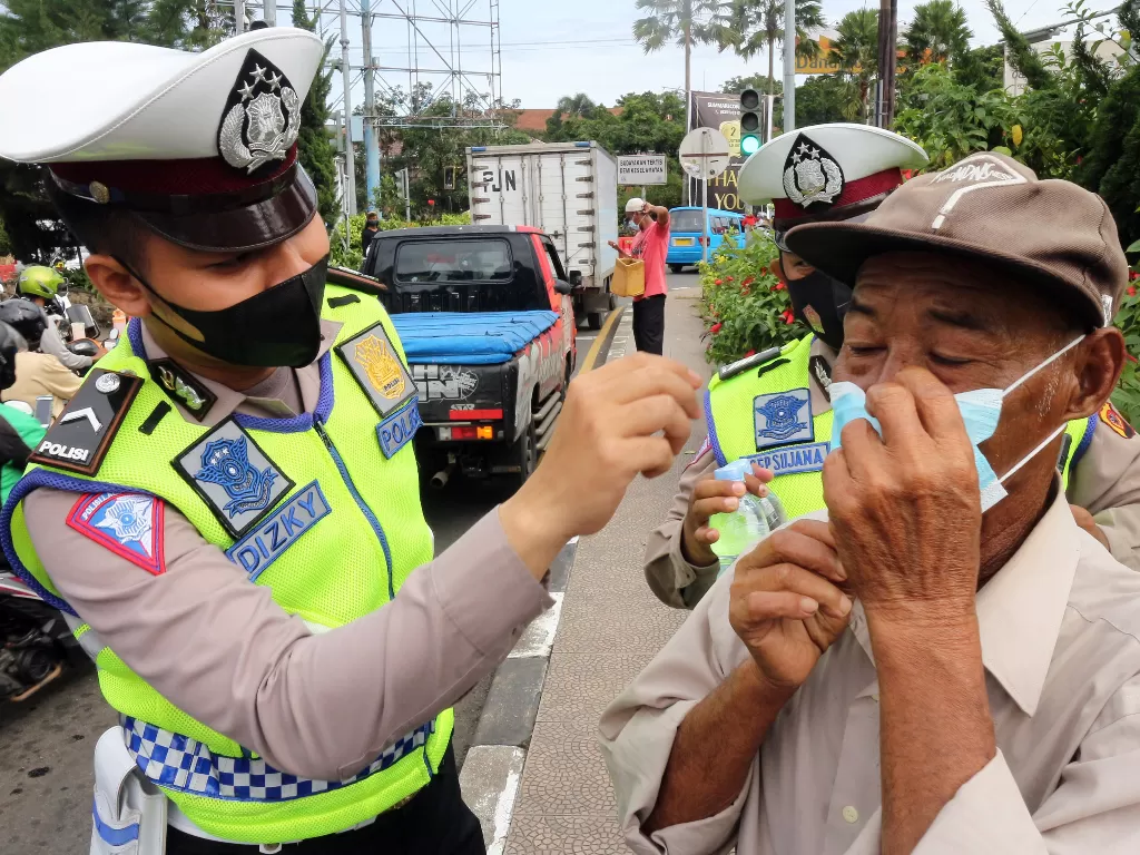 Petugas kepolisian membagikan masker kepada warga di Jalan Raya Puncak, Gadog, Kabupaten Bogor, Jawa Barat. (ANTARA FOTO/Yulius Satria Wijaya)