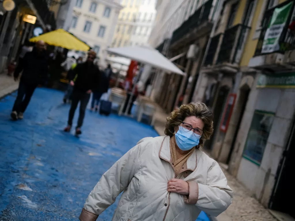 Seorang wanita mengenakan masker pelindung berjalan, beberapa saat sebelum konferensi pers pemerintah untuk mengumumkan pembatasan sosial. (REUTERS/Pedro Nunes)