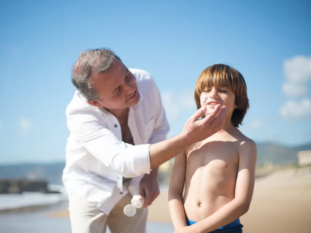 Ilustrasi anak kecil dipakaikan sunscreen saat di pantai. (Pexels/Kampus Production)
