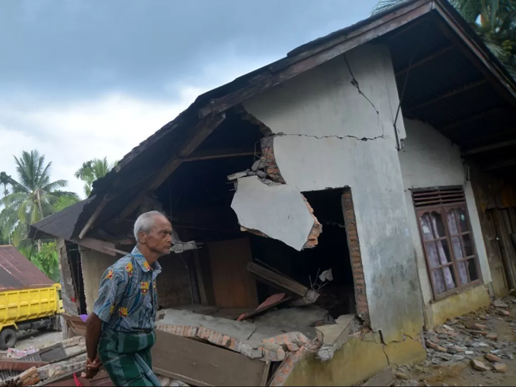 Warga melintas di depan rumah yang rusak akibat gempa di Jorong Pinagar,  Pasaman Barat, Sumbar. (ANTARA FOTO/Iggoy el Fitra)