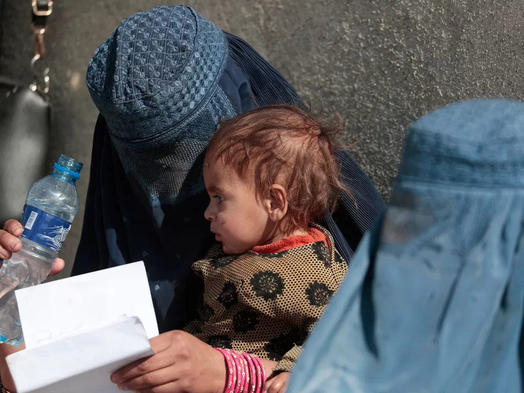 Wanita Afghanistan terlantar menggendong anaknya saat dia menunggu dengan wanita lain untuk menerima pasokan bantuan di luar pusat distribusi UNCHR di pinggiran Kabul, Afghanistan. (REUTERS/Zohra Bensemra)