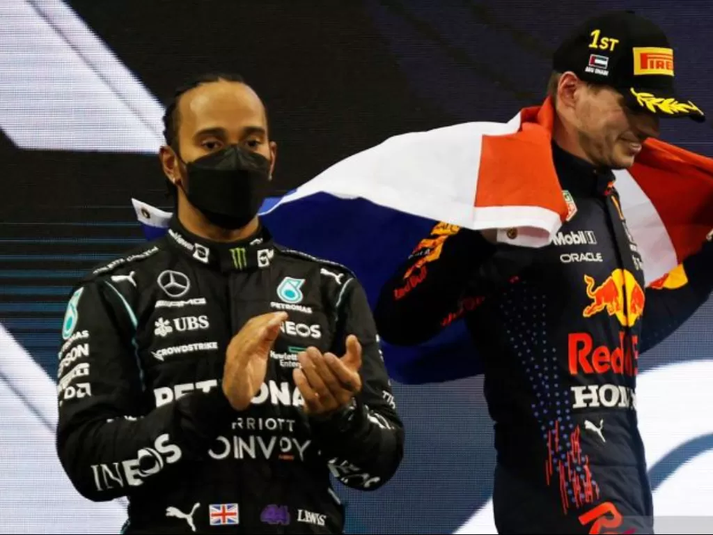 Pebalap Red Bull Max Verstappen merayakan kemenangan balapan dan kejuaraan dunia dengan bendera Belanda di podium saat pebalap Mercedes Lewis Hamilton terlihat setelah finis kedua selama Grand Prix Abu Dhabi di Sirkuit Yas Marina, Abu Dhabi, Uni Emirat Ar