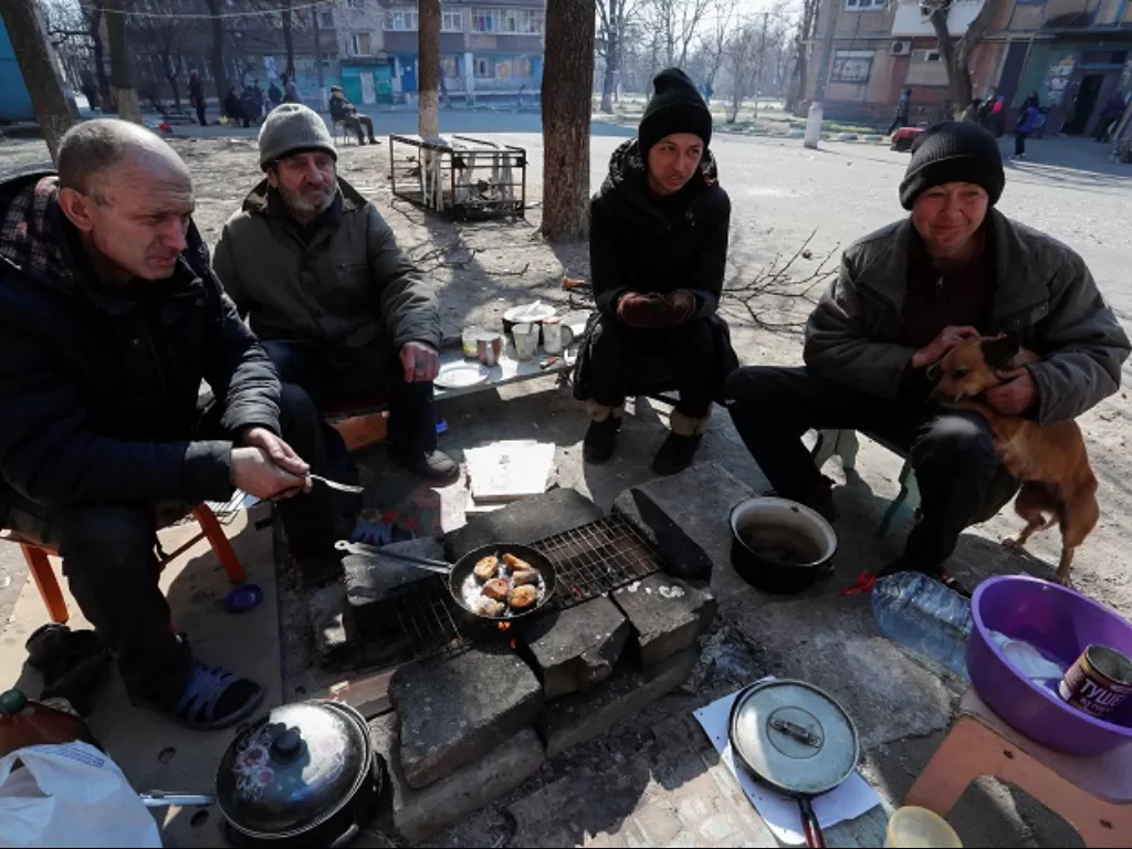 Warga Ukraina tengah memasak makanan kaleng untuk bertahan hidup dari invasi Rusia. (REUTERS/Alexander Ermochenko)