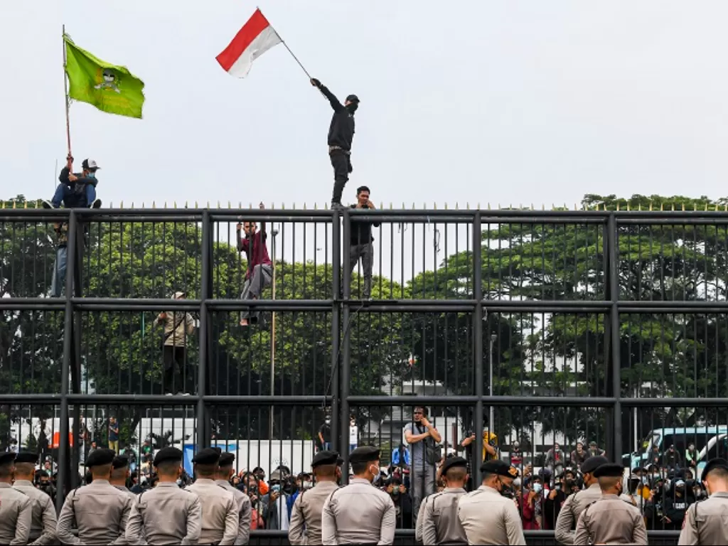Massa aksi mengibarkan bendera merah putih dengan menaiki pagar gedung DPR saat aksi unjuk rasa di depan kompleks Parlemen di Jakarta. (ANTARA FOTO/Galih Pradipta)