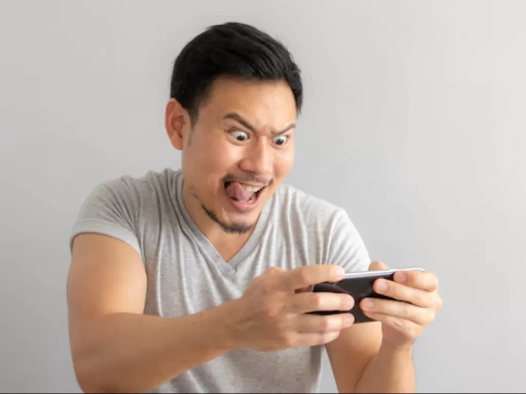 Ilustrasi pria yang sedang bermain game mobile. (Freepik)