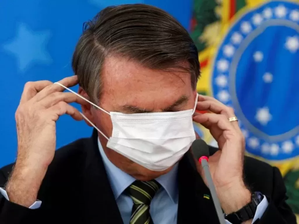Presiden Brasil Jair Bolsonaro memperbaiki maskernya saat memberikan keterangan media mengenai langkah pemerintah untuk mengendalikan penyebaran virus COVID-19 di Brasilia, Brasil, Rabu (18/3/2020). (REUTERS/ADRIANO MACHADO)