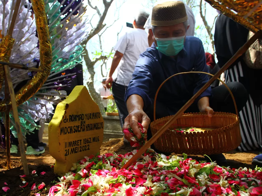Seorang pelayat menaburkan bunga di atas makam almarhum Achmad Yurianto di pemakaman umum Dadaprejo, Batu, Jawa Timur, Minggu (22/5/2022). (ANTARA/Ari Bowo Sucipto)