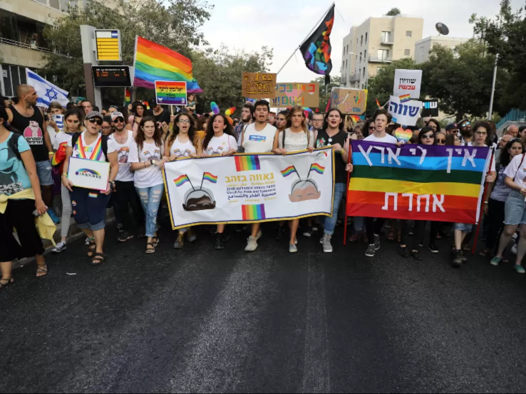 Para peserta memegang spanduk saat mereka ambil bagian dalam Parade Gay Pride tahunan ke-17 Yerusalem 2 Agustus 2018. Spanduk di sebelah kanan bertuliskan dalam bahasa Ibrani, 