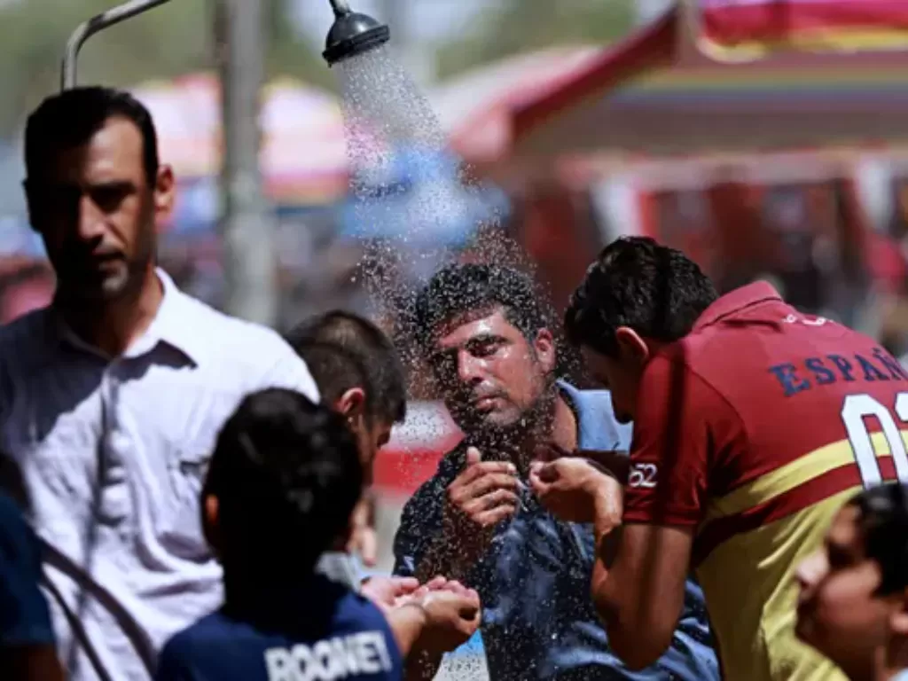 Orang-orang mendinginkan diri di bawah pancuran udara terbuka di Baghdad saat suhu panas. (The Guardian)