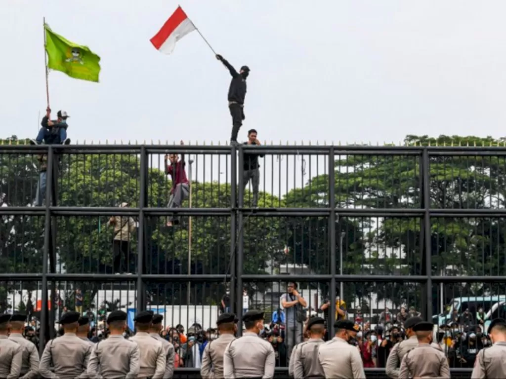 Massa aksi mengibarkan bendera merah putih dengan menaiki pagar gedung DPR. (ANTARA/Galih Pradipta)