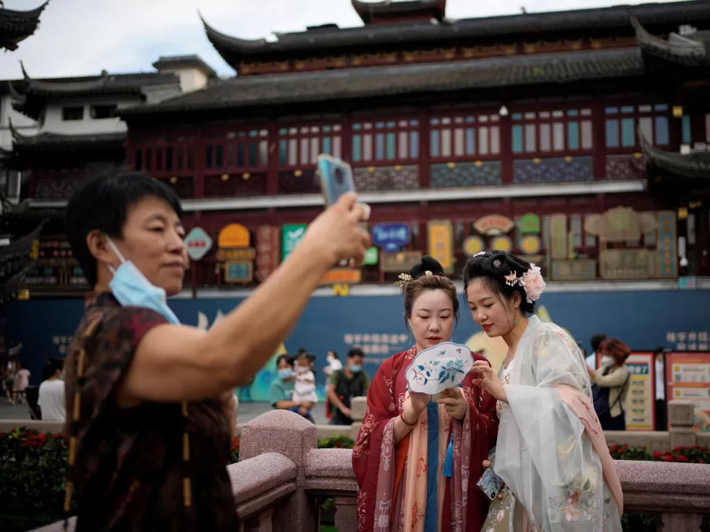 Wanita mengenakan gaun hanfu tradisional melihat telepon sebelum festival Pertengahan Musim Gugur di Taman Yu, setelah wabah penyakit coronavirus (COVID-19), di Shanghai, Cina , 9 September 2022. (REUTERS/Aly Song)