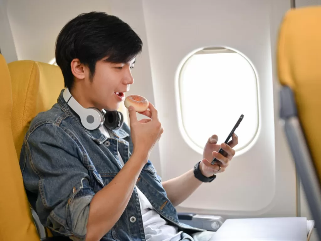 Ilustrasi penumpang pesawat menggunakan ponsel. (FREEPIK/thanyakij-12)