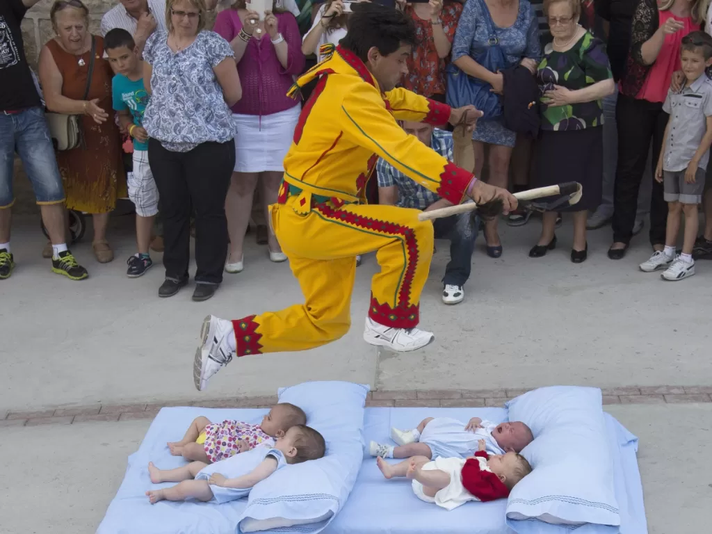 Seorang pria mengenakan kostum merah dan kuning yang mewakili iblis, yang dikenal sebagai El Colacho, melompati bayi yang diletakkan di atas kasur selama perayaan corpus christi tradisional di Castrillo de Murcia, dekat Burgos, Spanyol Utara. (REUTERS)