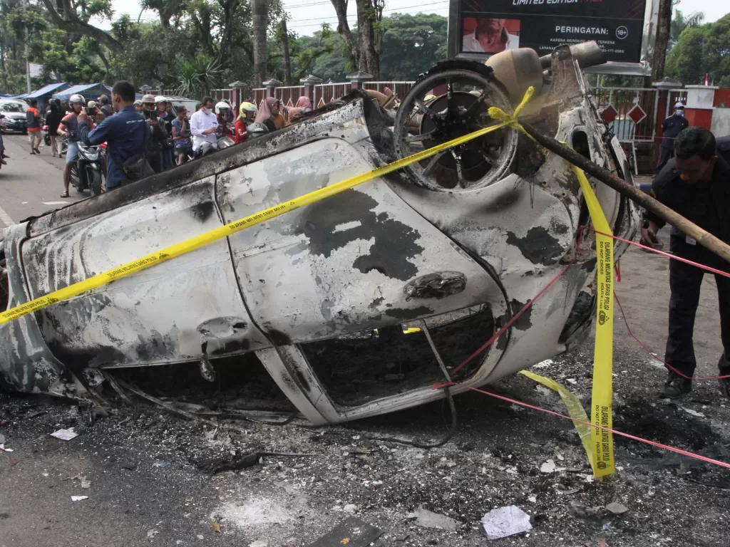 Seorang warga melintas di samping mobil yang terbakar pasca kerusuhan di Stadion Kanjuruhan, Malang, Jawa Timur, Minggu (2/10/2022). Polda Jatim mencatat data sementara korban jiwa dalam kejadian tersebut berjumlah 127 orang dan 13 kendaraan rusak. (ANTAR