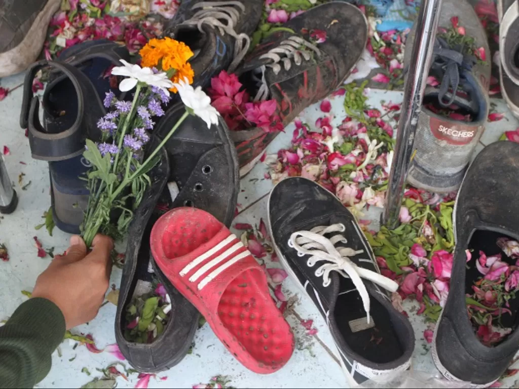 Suporter Arema FC (Aremania) meletakkan bunga di atas alas kaki para korban yang tertinggal di depan pintu tribun 11 Stadion Kanjuruhan. (ANTARA FOTO/Ari Bowo Sucipto)