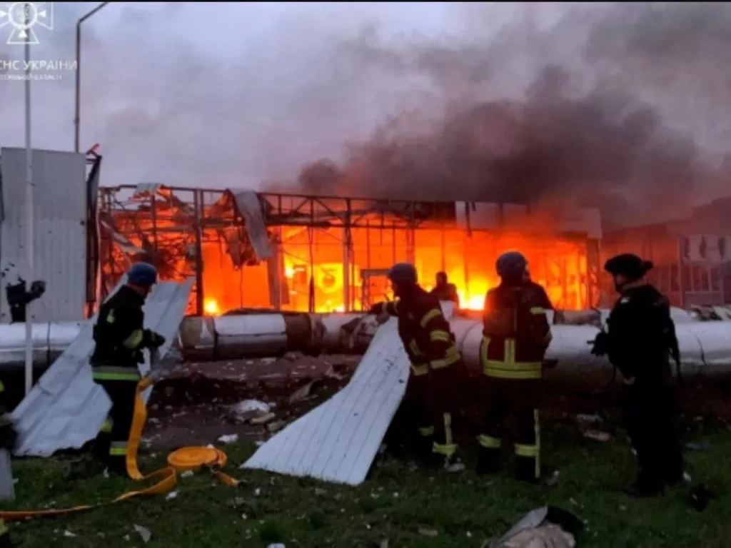 Petugas pemadam kebakaran bekerja di lokasi dealer mobil yang hancur selama serangan rudal Rusia di Zaporizhzhia (Handout via Reuters)