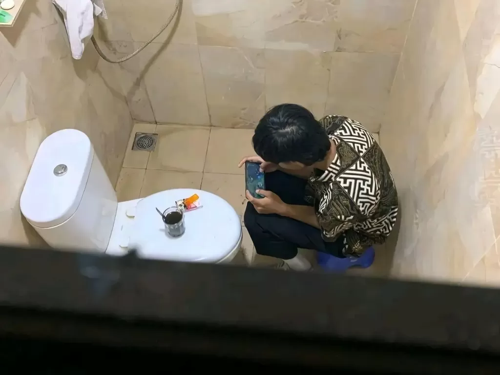 Pria yang sedang pushrank Mobile Legends di toilet lengkap dengan kopi dan rokok. (Twitter/@ndagels)