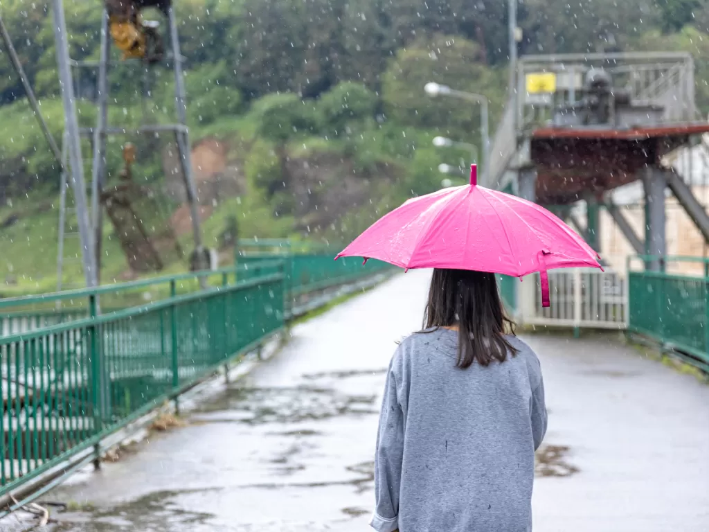 Ilustrasi perempuan gunakan payung di bawah hujan. (Freepik/pvproductions)