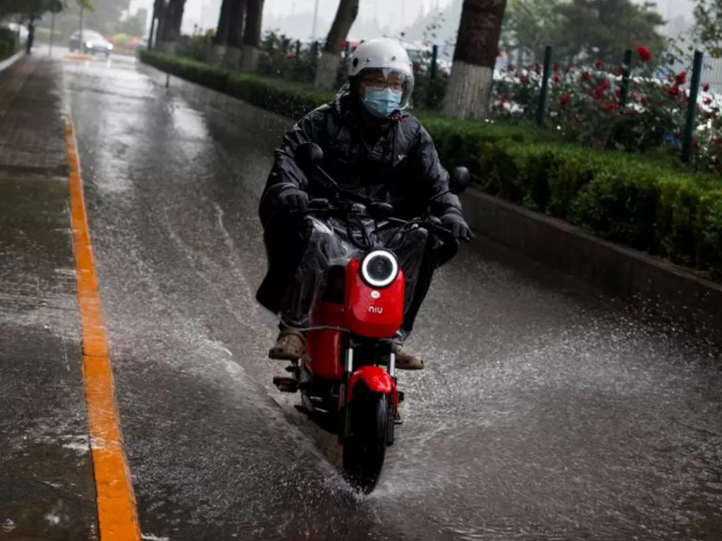 Pengendara sepeda motor listrik sedang mengenakan jas hujan saat hujan deras. (REUTERS/Thomas Peter)