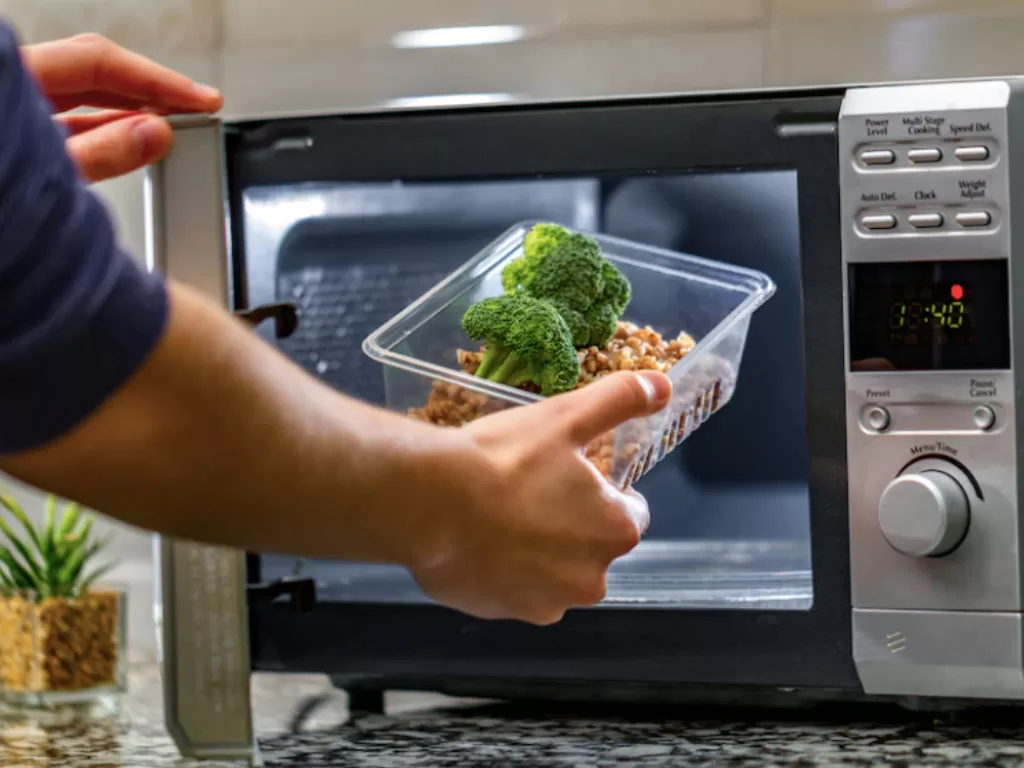 Ilustrasi seseorang yang memanaskan makanan di microwave yang diduga bisa picu sel kanker. (Freepik)