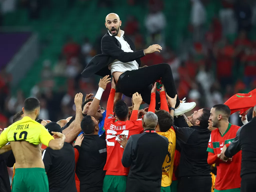 Pelatih Maroko, Walid Regragui, dilempar ke udara oleh para pemainnya usai lolos ke semifinal Piala Dunia 2022. (REUTERS/Carl Recine)