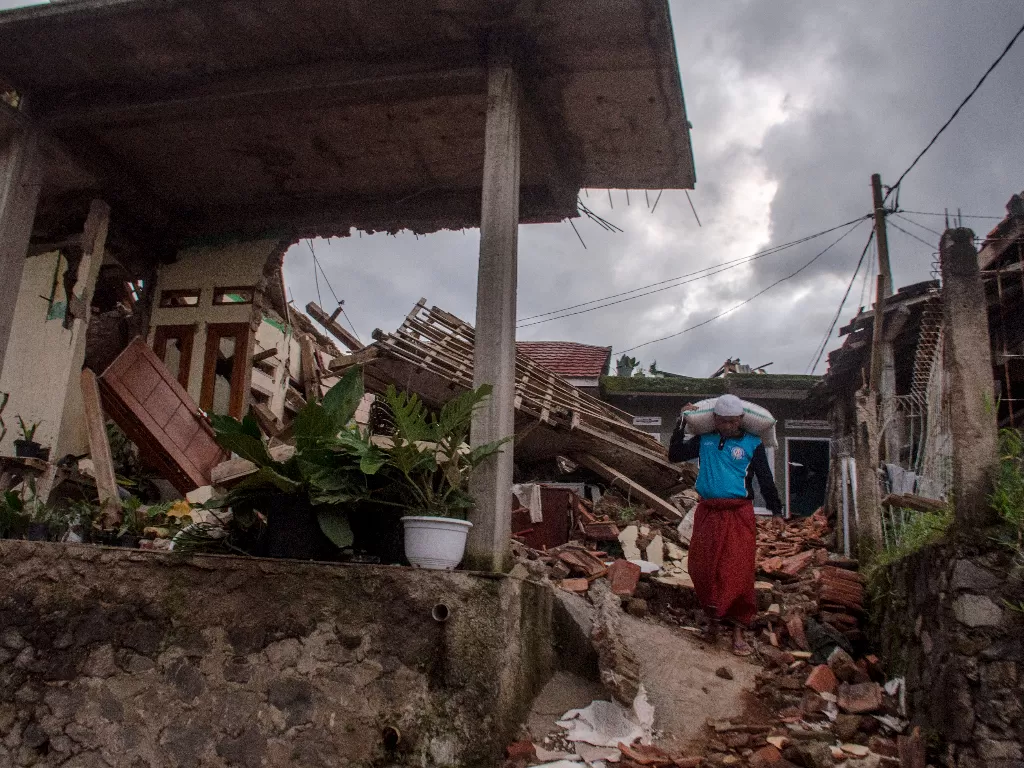 Warga membawa beras di dekat rumah yang rusak akibat gempa bumi di Gasol, Cianjur, Jawa Barat. (ANTARA/Novrian Arbi)