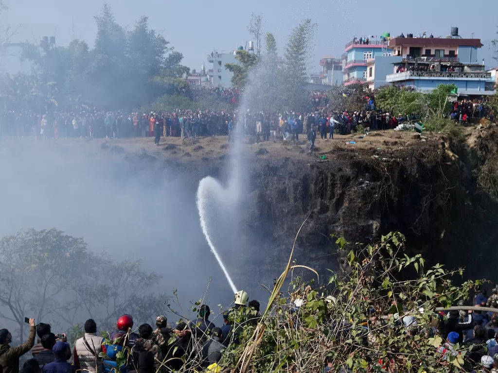 Pasukan pemadam kebakaran menyemprotkan air untuk memadamkan api di lokasi jatuhnya pesawat yang membawa 72 orang di Pokhara di Nepal barat 15 Januari 2023. (REUTERS/Rohit Giri )