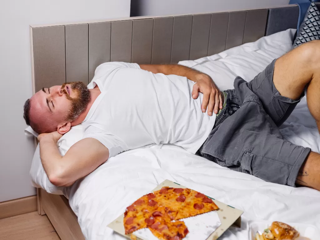 Ilustrasi pria makan sambil tidur. (Freepik)