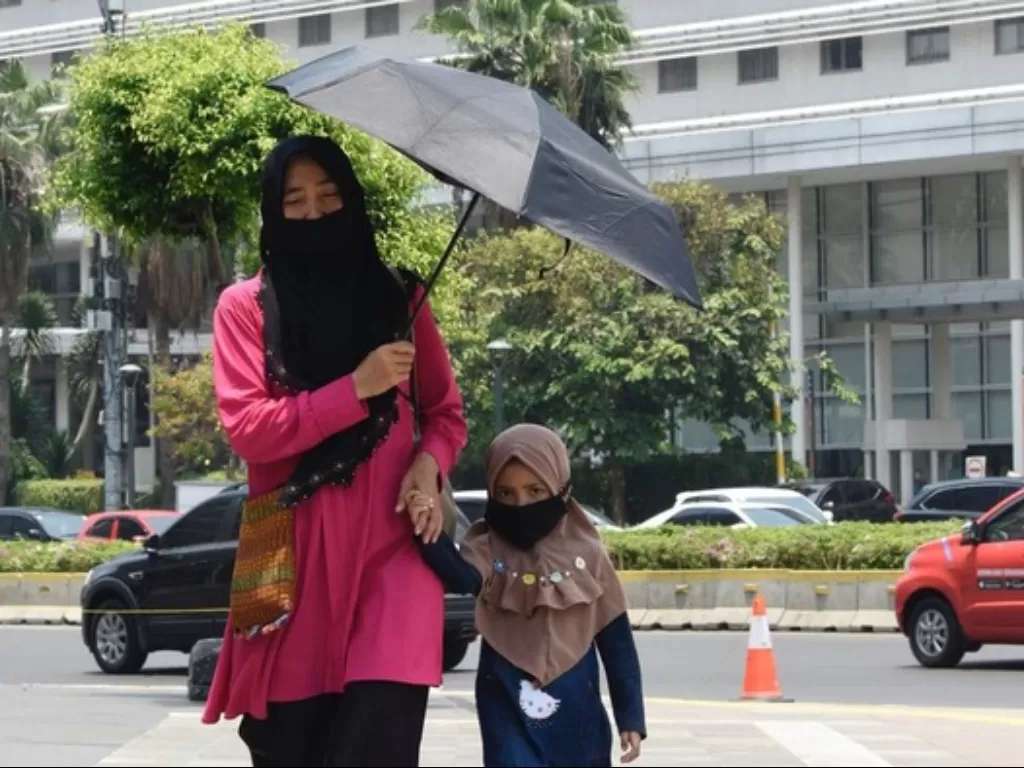 Ilustrasi - eorang bersama anaknya menggunakan payung untuk menghindari sengatan matahari ketika berjalan di sekitar Bunderan HI, Jakarta, Rabu (23/10/2019). (ANTARA FOTO/Saptono)