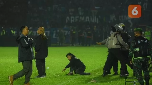 Seorang Aremania terjatuh di lapangan Stadion Kanjuruhan dan pihak kepolisian berusaha mengamankan. (Iwan Setiawan/Bola.com