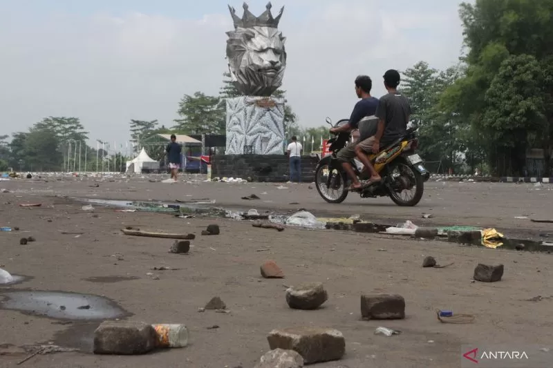 Seorang pengendara motor melintas diantara puing batu yang dilemparkan suporter dalam kerusuhan di Stadion Kanjuruhan, Malang, Jawa Timur, Minggu (2/10/2022). Polda Jatim mencatat data sementara korban jiwa dalam kejadian tersebut berjumlah 127 orang dan 13 kendaraan rusak.