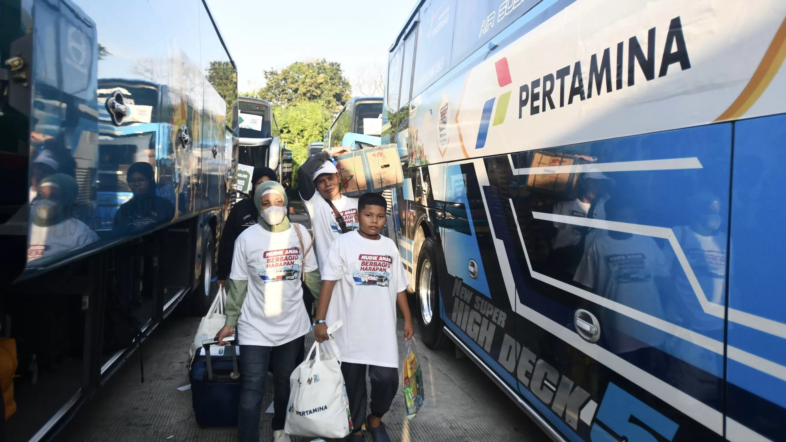Sejumlah pemudik melintas di samping bus tujuan malang saat Kegiatan Pertamina Mudik Aman Berbagi Harapan 2026 yang diselenggarakan di Lapangan Teater Keong Mas, TMII, Jakarta, Minggu (15/03/2026).