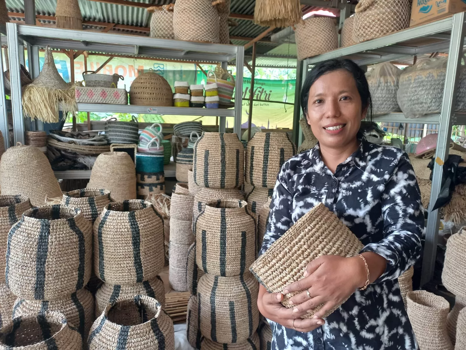 Yu Payem dengan latar produk kerajinan anyaman serat alam di Showroomnya. (Foto: Agusigit)