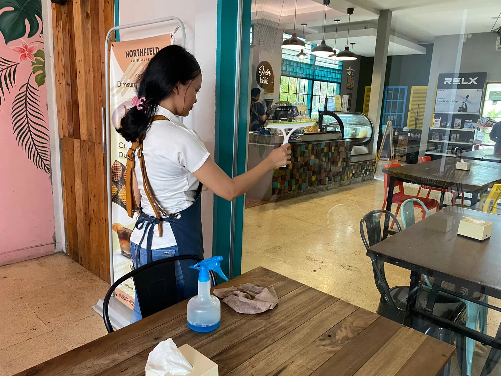 Seorang petugas kafe sedang membersihkan kaca jendela. (Pande / Rinus Muntu)