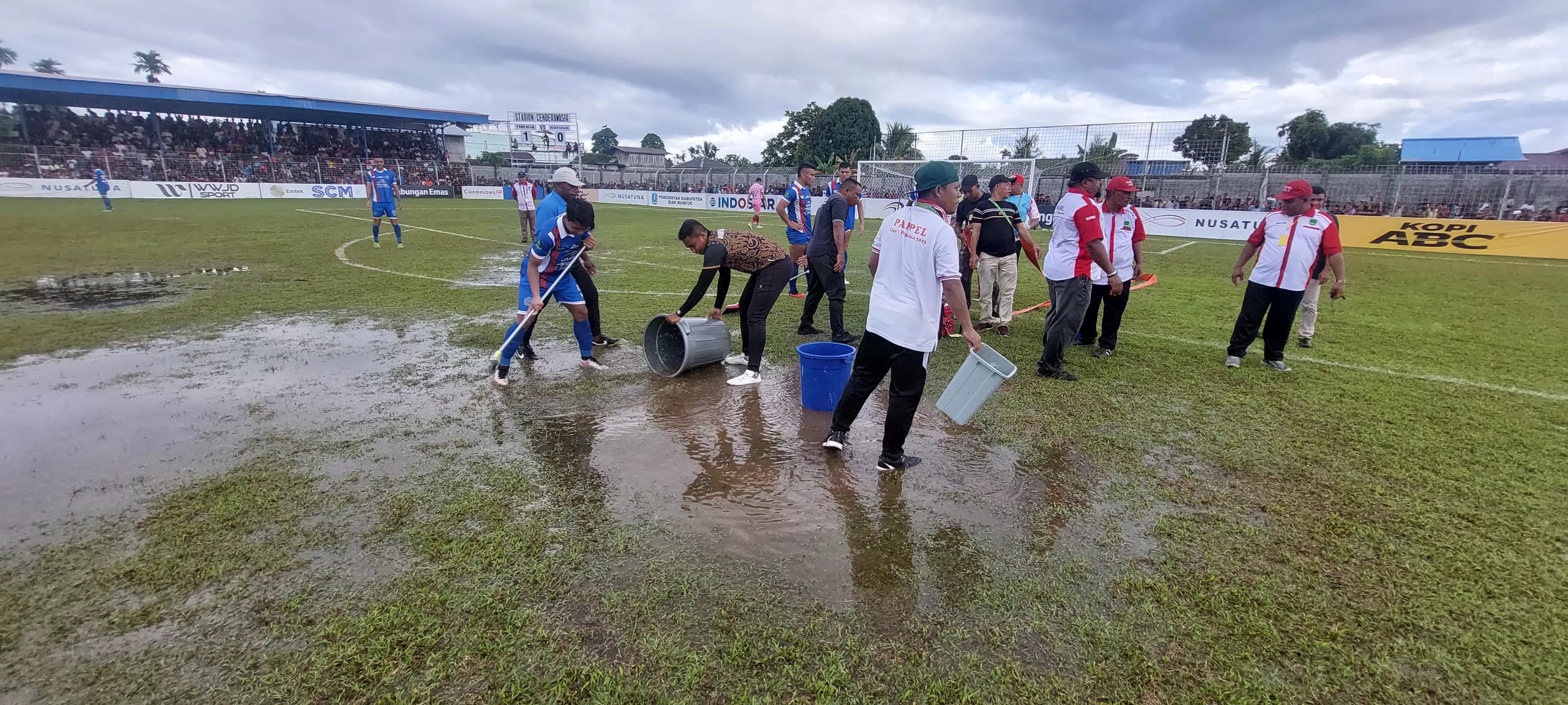 Panitia pertandingan membersihkan lapangan Stadion Cenderawsih dari genangan air akibat hujan deras di laga Final Liga 2, Selasa (5/3/2024). (MO PSBS BIAK)