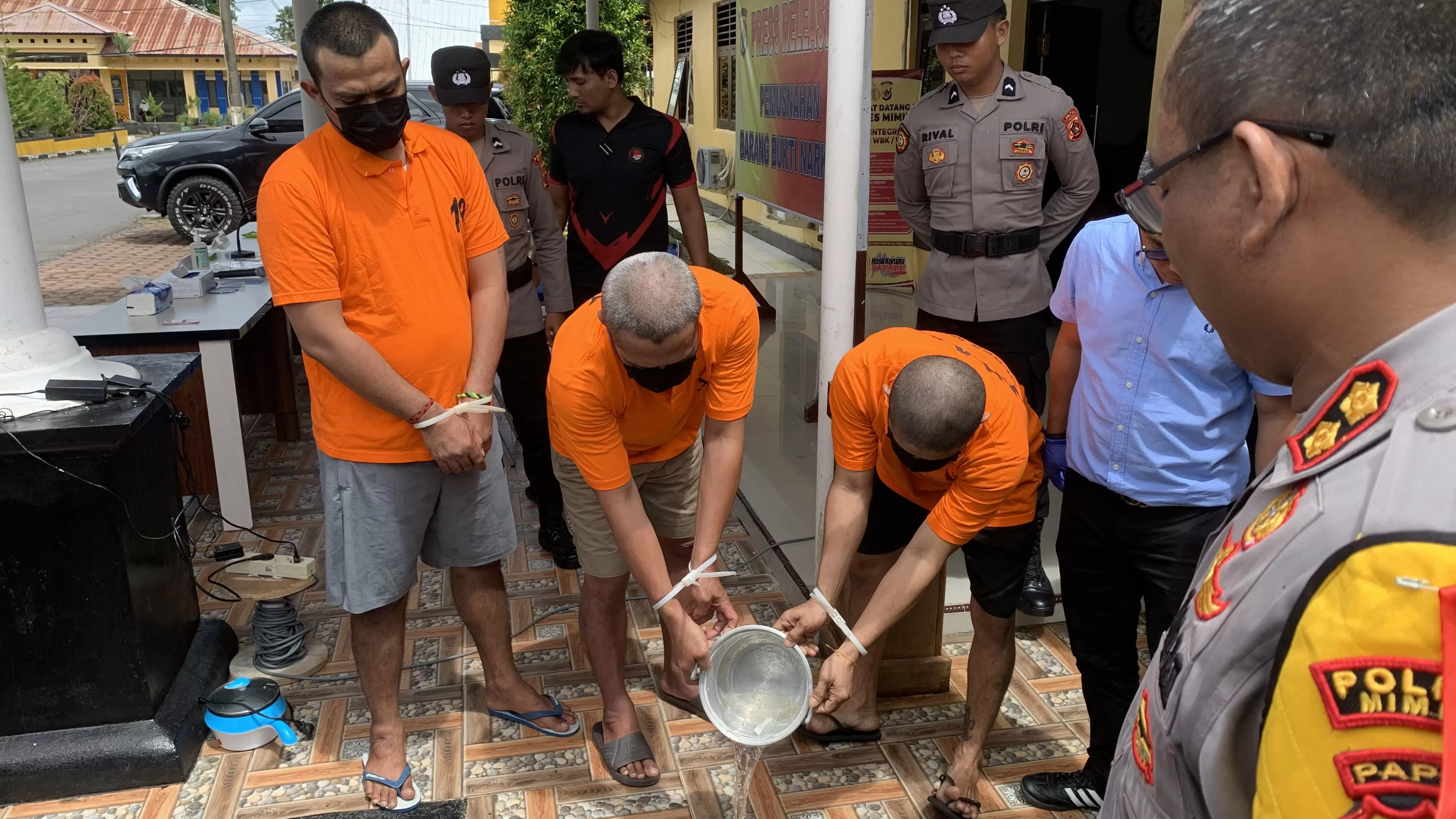 Tiga tersangka tindak pidana narkotika sedang menuangkan barang bukti narkotika jenis sabu yang dilarutkan di dalam panci berisikan air panas ke dalam selokan, disaksikan jajaran Forkopimda. (CENDERAWASIH POS/Wahyu Welerubun)