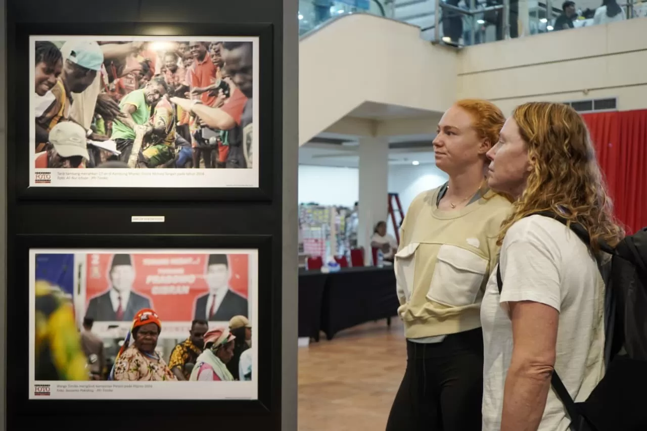Dua orang pengunjung mancanegara sedang melihat arsip perjalanan Kabupaten Mimika yang dipajang di pameran foto. (Dokumen PFI Kota Timika).