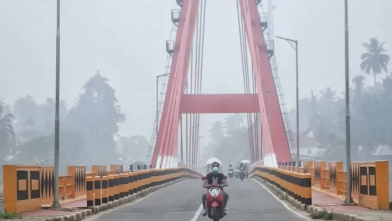 Warga melintasi Jembatan Kabel Dharmasraya di tengah kabut asap. (Foto: Desrian)