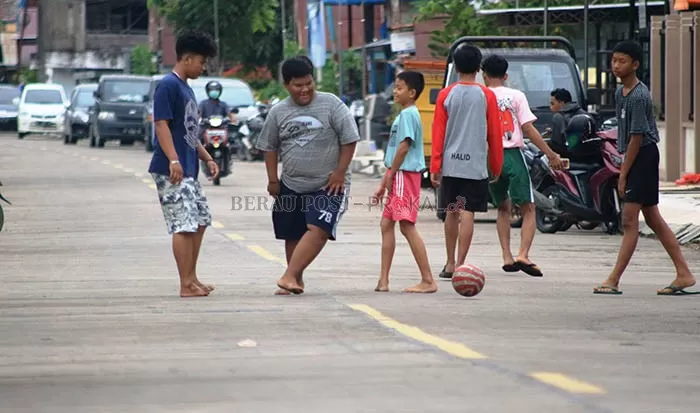 HARUSNYA DI RUMAH: Para anak-anak sekolah tampak sedang asik bermain bola di ruas jalan, meskipun pemerintah telah meminta agar tetap beraktifitas di dalam rumah.