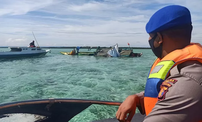 TERBALIK: Personil Polairud bersama anggota Pospol Batu Putih melakukan evakuasi kapal nelayan yang terbalik diterjang ombak.