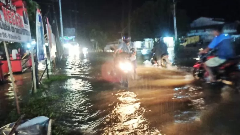 Seorang warga terpaksa mendorong sepeda motornya melewati banjir di depan jembatan Ngabang, Jumat (15/1). Akses jalan Ngabang - Sanggau pun hampir terputus.