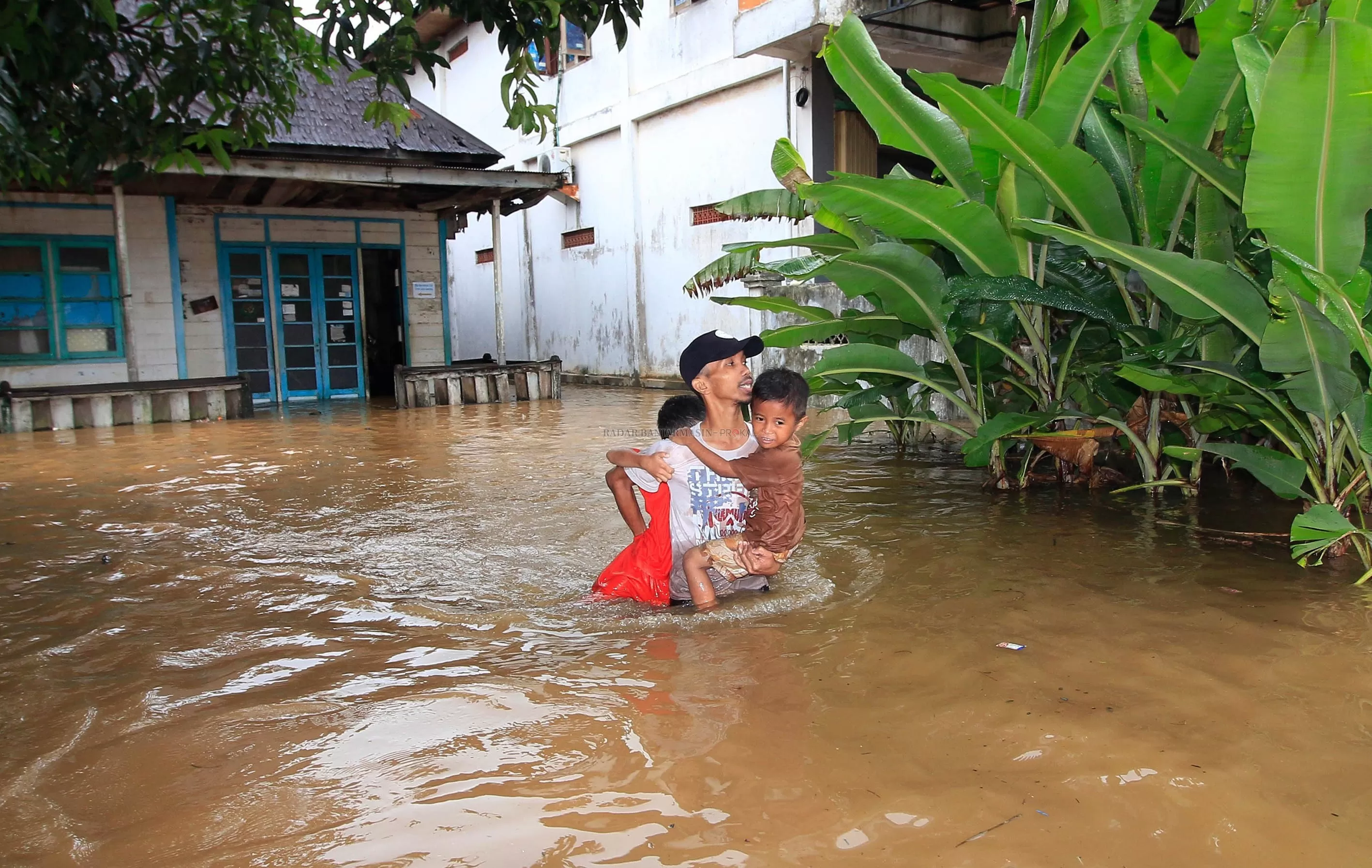 GENDONG ANAK: Seorang Bapak menggendong anaknya. Banjir kemarin pagi membuat 20 RT di Cempaka dan Sungai Tiung terendam. | FOTO: MUHAMMAD RIFANI/RADAR BANJARMASIN