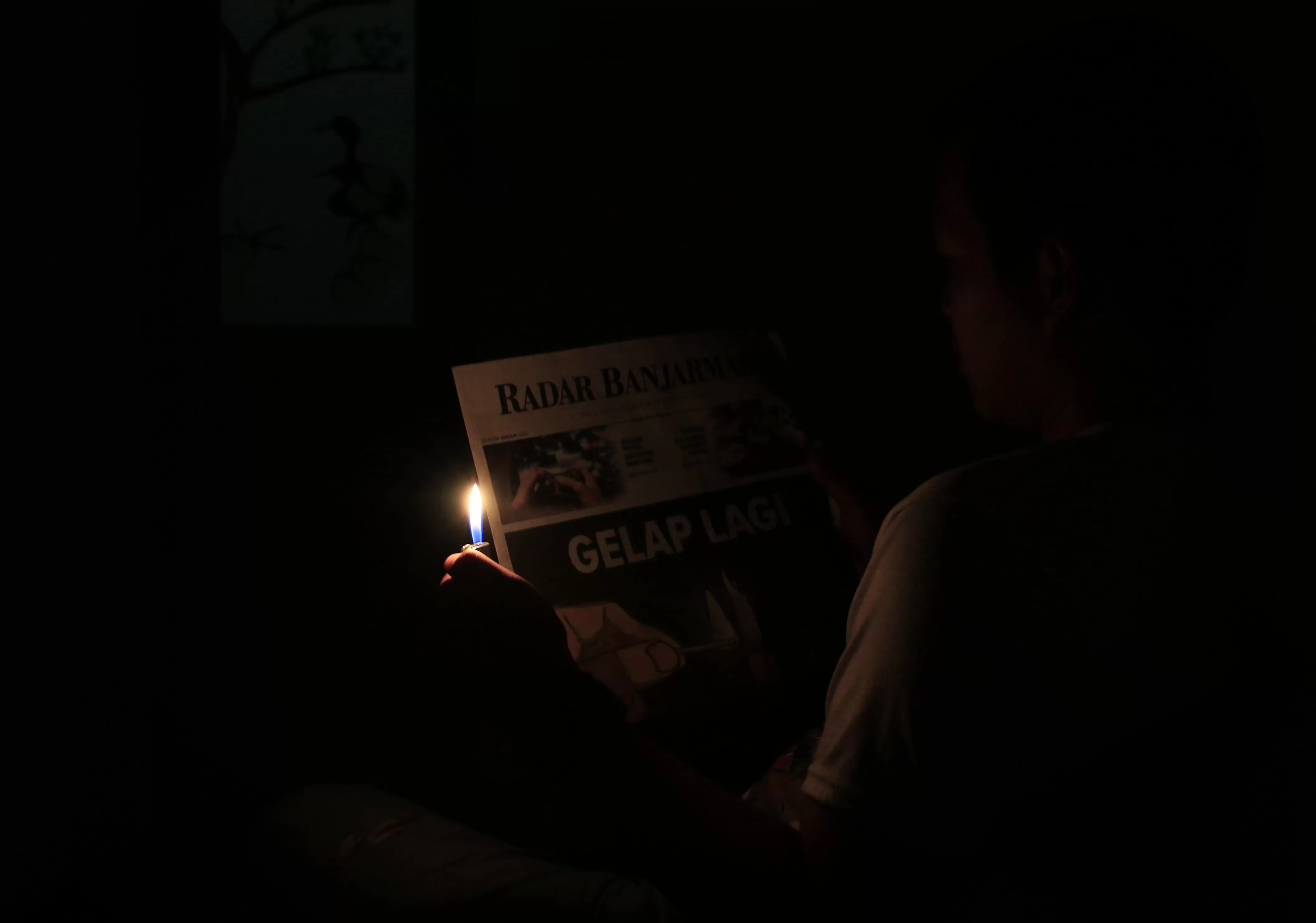 BERMODAL KOREK: Salah seorang warga Banjarbaru terpaksa menggunakan penerangan minim untuk membaca koran kala listrik di wilayahnya padam akibat adanya gangguan transmisi di PLN Kalselteng.| Foto:  Muhammad Rifani/RADAR BANJARMASIN