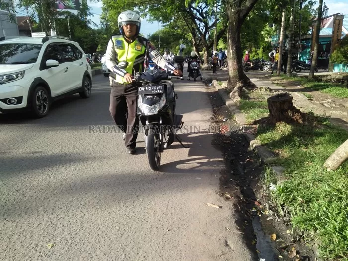 KENA JUGA: Polantas menggiring sepeda motor yang ditinggalkan pemiliknya entah ke mana. Banyak pengendara yang menghindari razia dengan pura-pura parkir di sekitar kantor Samsat. | FOTO: MAULANA/RADAR BANJARMASIN