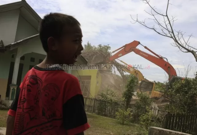 BERTERIAK: Seorang anak menyaksikan proses eksekusi rumah oleh alat berat ekskavator pada Rabu (19/2) di kawasan Landasan Ulin Barat Kecamatan Landasan Ulin Banjarbaru. Eksekusi ini akan merobohkan 11 rumah warga yang dilakukan oleh pihak Pengadilan Negeri Banjarbaru. | Foto: Muhammad Rifani/Radar Banjarmasin