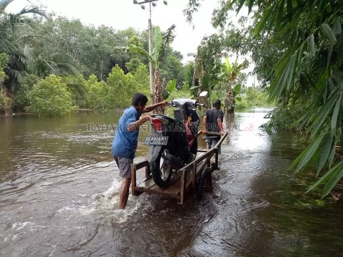 DIANGKUT GEROBAK: Warga Desa Binturu meminta bantuan warga lainnya untuk mengangkut kendaraannya ke gerobak agar bisa melintasi banjir.