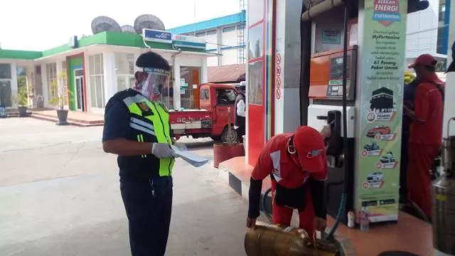 TETAP BERTUGAS: Dengan mengenakan face shield, petugas Disdag Kota Banjarbaru menera alat pengisi BBM di SPBU Liang Anggang.