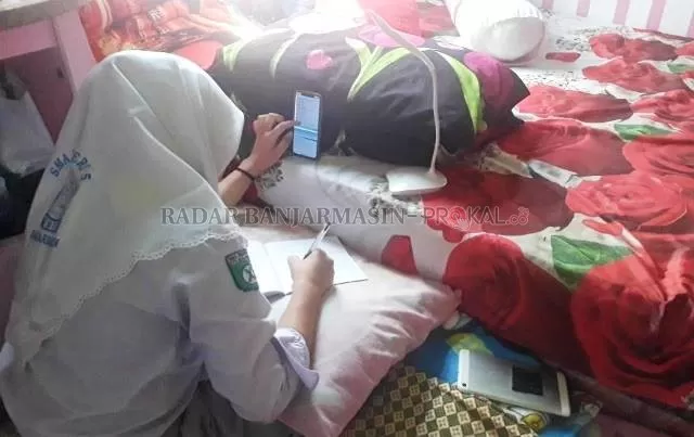 BELAJAR DARING: Siswi di Banjarmasin belajar daring. Sekalipun belajar di kamar tidur, siswi ini tetap mengenakan seragam lengkap. | Foto: Endang/Radar Banjarmasin