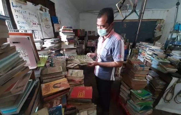JENDELA DUNIA: Johan, 45 tahun, difoto Senin (19/10) siang di antara tumpukan buku bekas jualannya. | Foto: Wahyu Ramadhan/Radar Banjarmasin