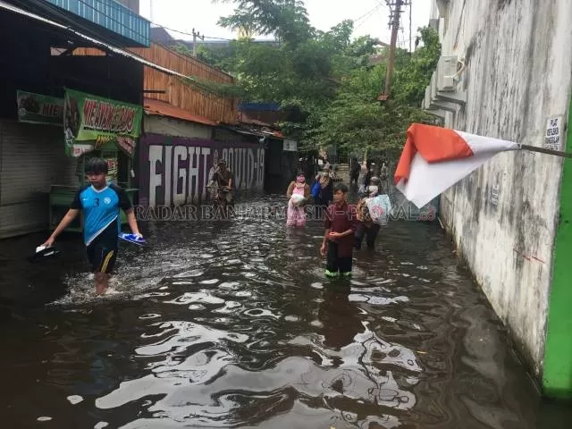 LAMBAT SURUT: Warga Banjarmasin melintasi jalanan yang masih tergenang di kompleks dekat Jalan Kuripan. Banjir tak surut meski hujan tak lagi turun. | FOTO: M OSCAR FRABY/RADAR BANJARMASIN